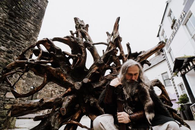 A viking kneeling to the ground beside the base of a wooden sculpture